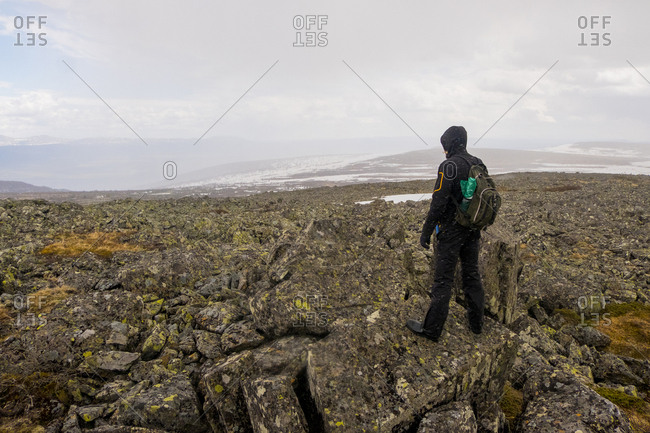 Rear view of hiker looking at view while standing on mountain cliff against cloudy sky