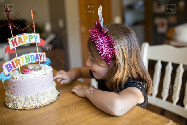 High angle view of girl touching birthday cake while sitting on chair at home