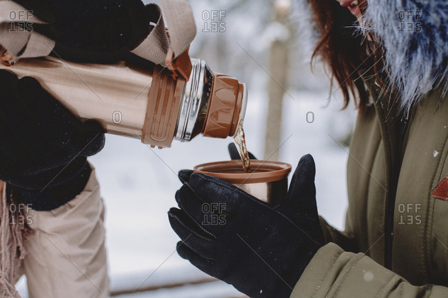 Midsection of lesbian woman pouring tea for wife in cup at park during winter