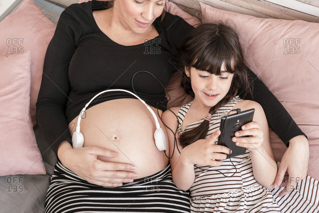 daughter playing music on mother pregnant belly