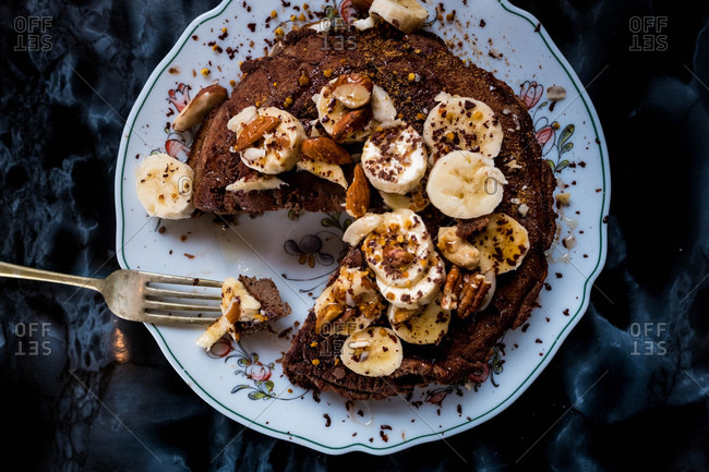 A forkful of cacao pancakes covered in banana, nuts and honey