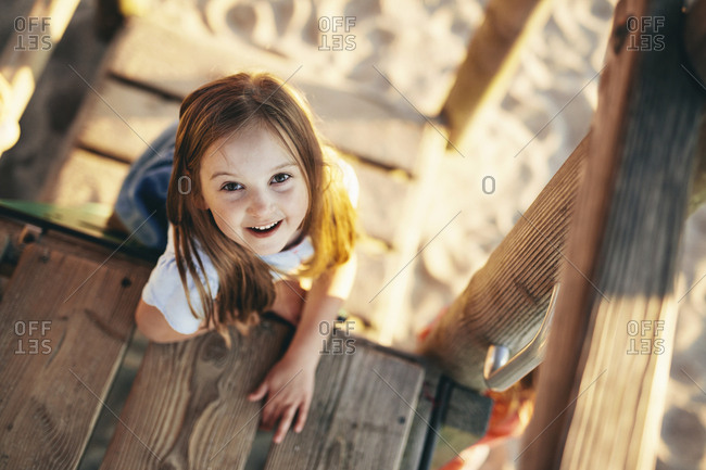 High angle portrait of happy girl sitting on wooden outdoor play equipment at playground during sunset