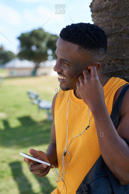 African american man using smartphone listening to music relaxing outdoors in park enjoying summer