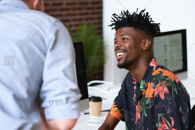 Happy african american man talking to colleague in office smiling happy wearing Hawaiian shirt