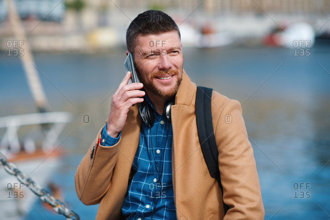 Businessman man using smartphone having phone call talking on mobile phone in waterfront harbor