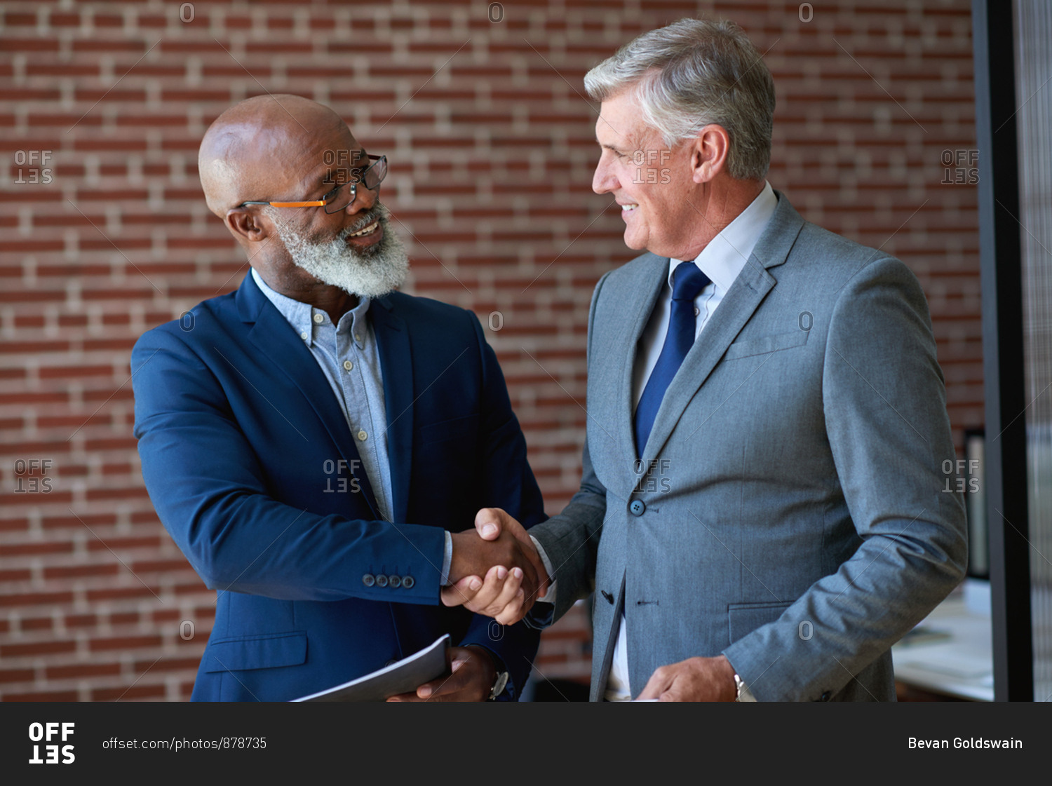 Two businessmen shaking hands in office handshake for successful partnership deal