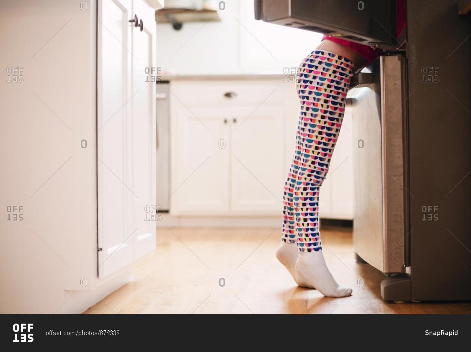Girl looking for food in an open refrigerator in the kitchen
