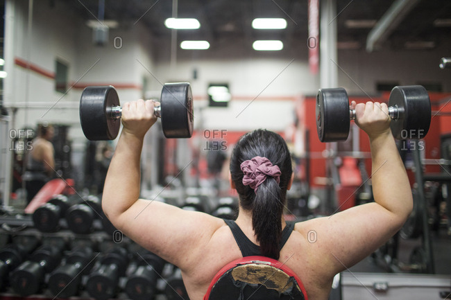 Rear view of strong woman exercising with dumbbells  at the gym.