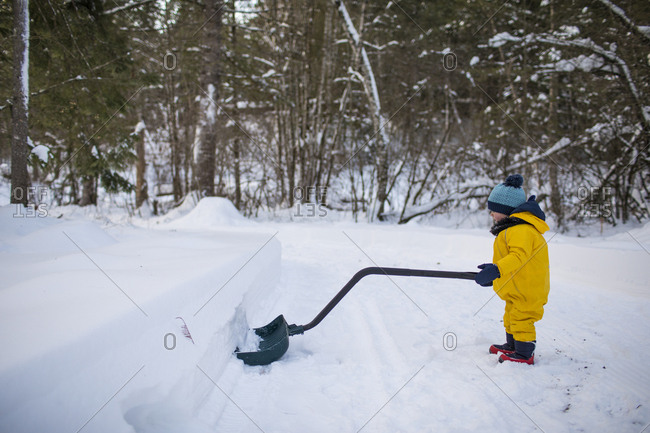 Toddler uses a large snow shovel to clear snow off the driveway.