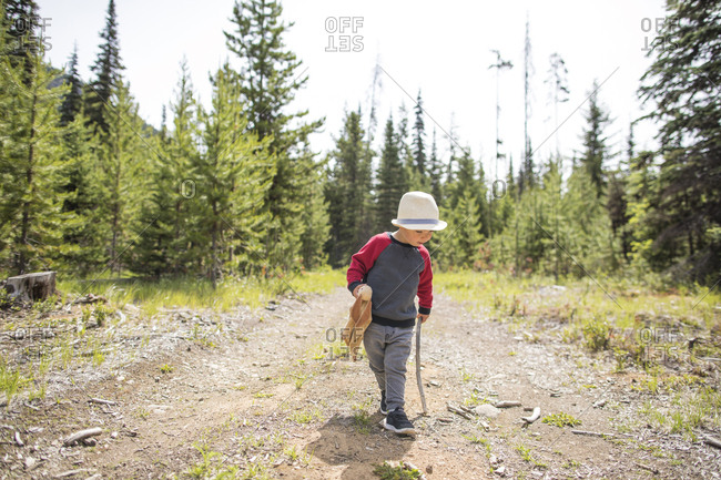 Young care-free boy walking on dirt path with walking stick and bunny