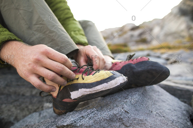 Rock climber laces up his worn climbing shoes