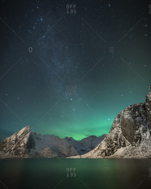Scenic view of calm lake by mountains against star field during winter at night