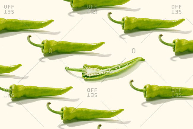 From above creative composition of sliced green pepper with seeds among whole peppers on white surface