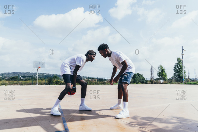 Side view of African American guys playing basketball in bright day on play ground
