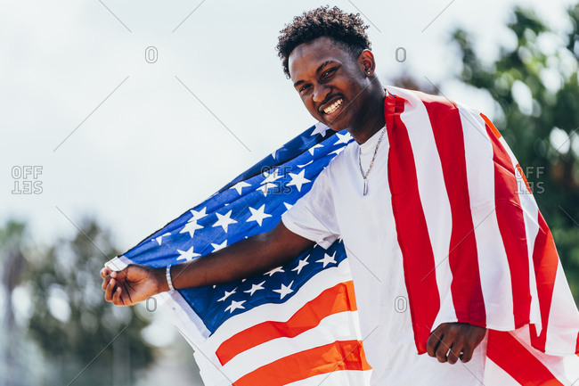 Serious African American man holding American flag on shoulder and looking away