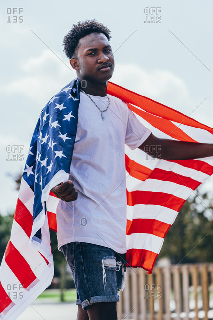 Serious African American man holding American flag on shoulder and looking away