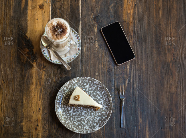 Cup of coffee, slice of cake, and phone on a table