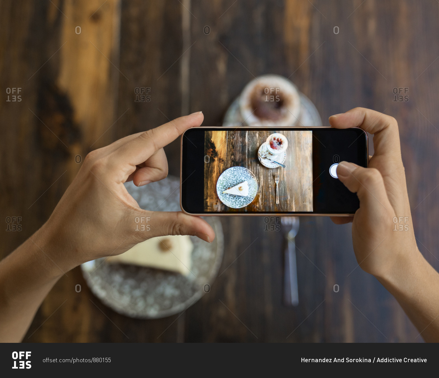 Unrecognizable woman taking photo by smartphone of piece of cake on plate with ornament and served coffee on wooden table
