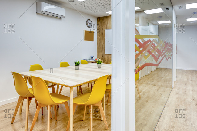 Light corridor with wooden floor among glass walls of light modern cozy office conference zones with comfortable yellow chairs at big wooden tables