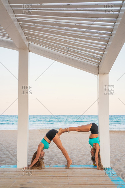 Sportive women doing acrobatic yoga posture double dog down on sandy beach