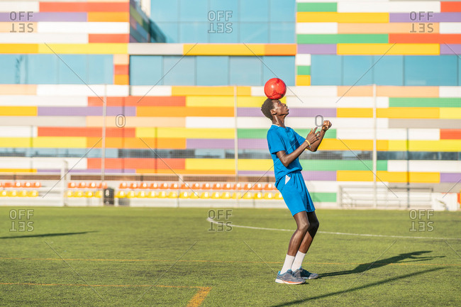 Skinny black teenager jugging football ball on head