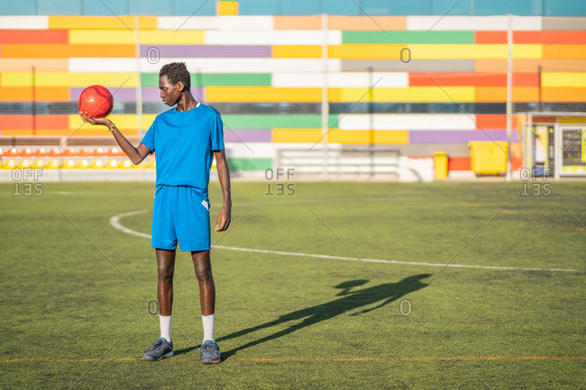 Black teenager with football ball against sky