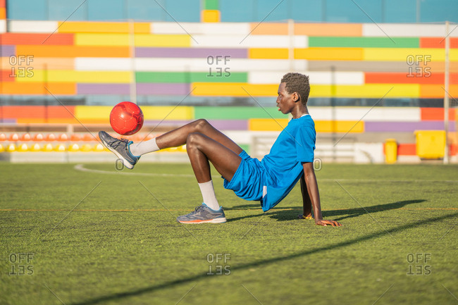 Side view of ethnic football player leaning back and juggling ball on foot during workout on stadium