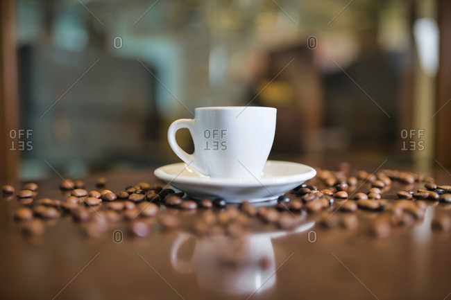 Ceramic cup on round saucer among roasted coffee beans on wooden table