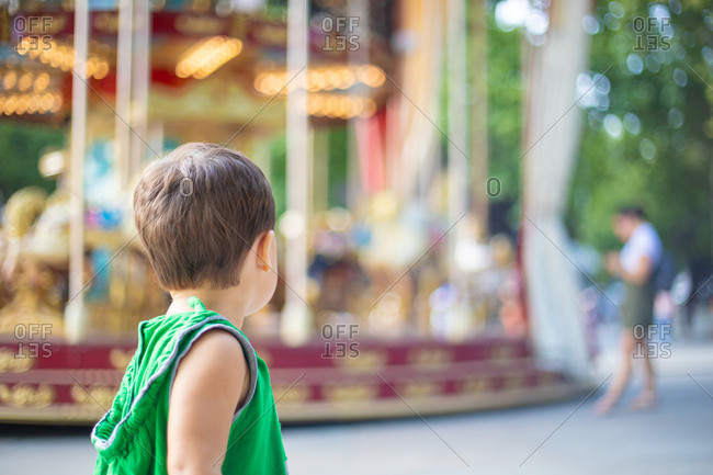 Child watching moving carousel and dreaming at fair