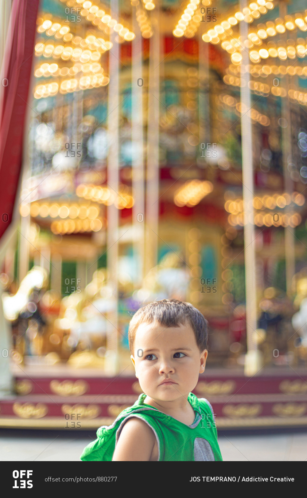 Child standing near moving carousel and dreaming at fair