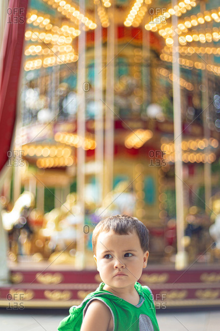 Child standing near moving carousel and dreaming at fair