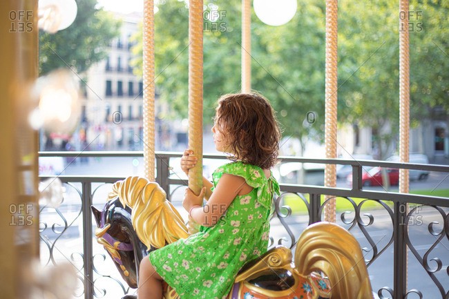 Charming little girl on colorful moving merry go round at fair in daylight