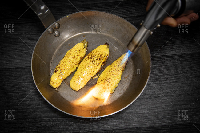 Crop person directing burner to pan with juicy endive preparing in frying pan on gray background