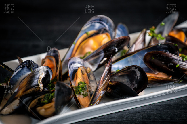 Fresh appetizing steamed mussels with Thai sauce decorated with basil in white plate on table