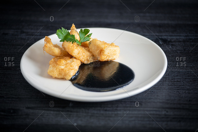 Fresh appetizing Hake breaded with squid cream in white plate on gray background