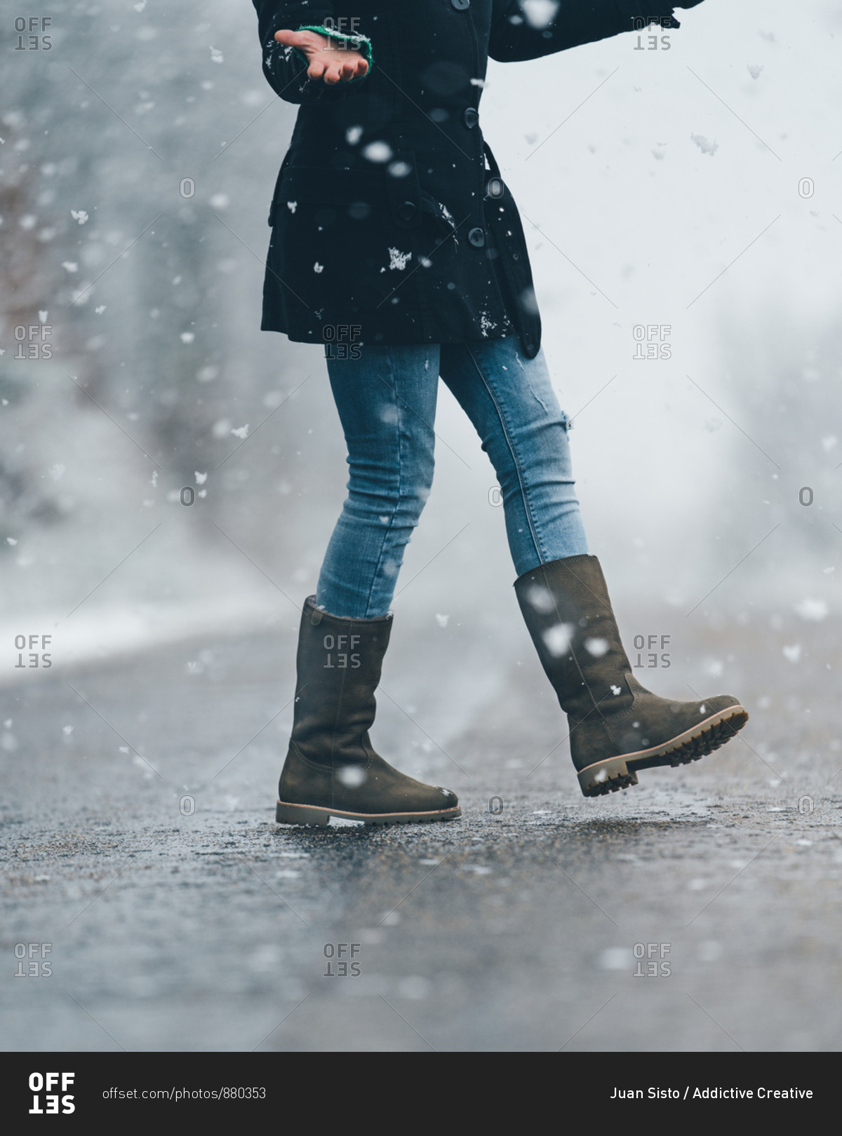 Side view of lonely female in black jacket and jeans crossing empty country road on snow and gloomy winter day