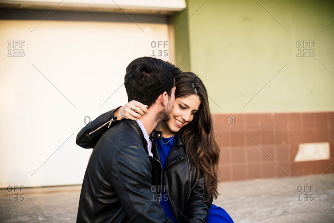 Loving man and woman in elegant clothes kissing on street background