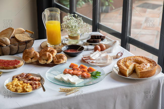 From above of appetizing sitting table for breakfast with bakery seafood sandwiches eggs and orange juice at stylish dinning room