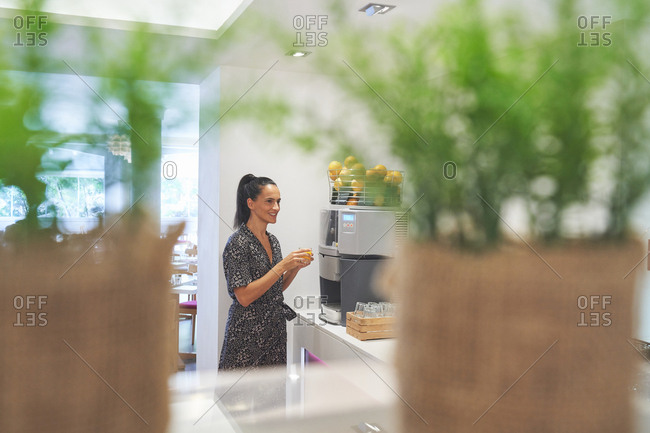 Side view of active slim woman loading citrus into big juicer for preparing drink in spacious room