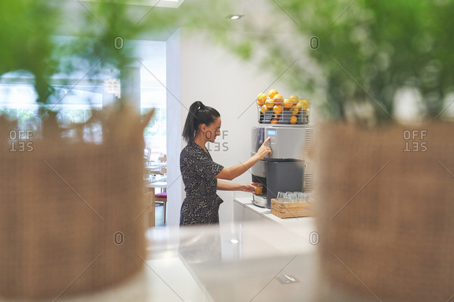 Side view of active slim woman loading citrus into big juicer for preparing drink in spacious room