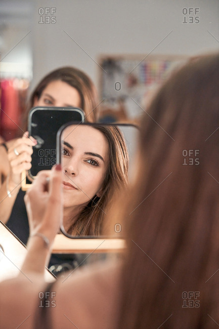Reflection of a beautiful woman face in mirror in hand of smiling lady after cosmetic procedure in salon