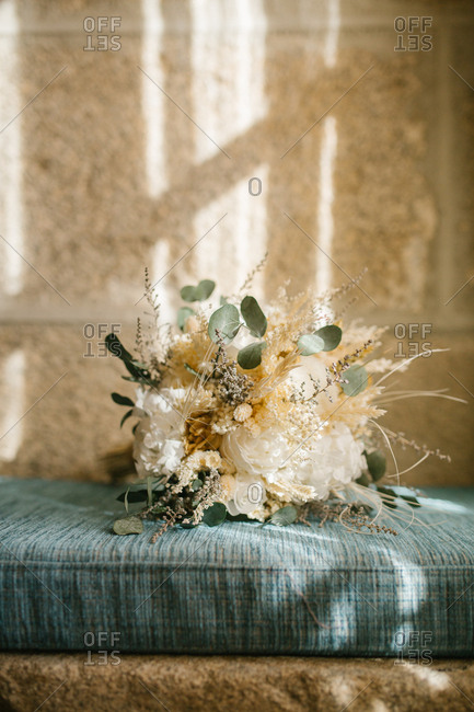Bunch of delicate white flowers placed on blue rustic cushion near window at home