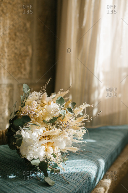 Bunch of delicate white flowers placed on blue rustic cushion near window at home