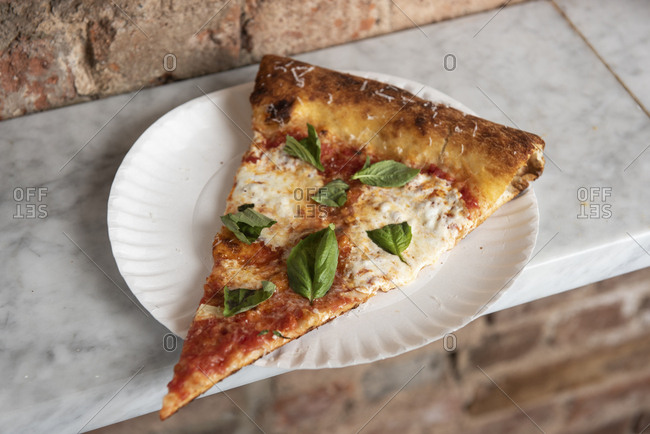 Slice of margherita pizza on a paper plate