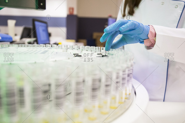 Close up of gloved hand picking up test tube from rack