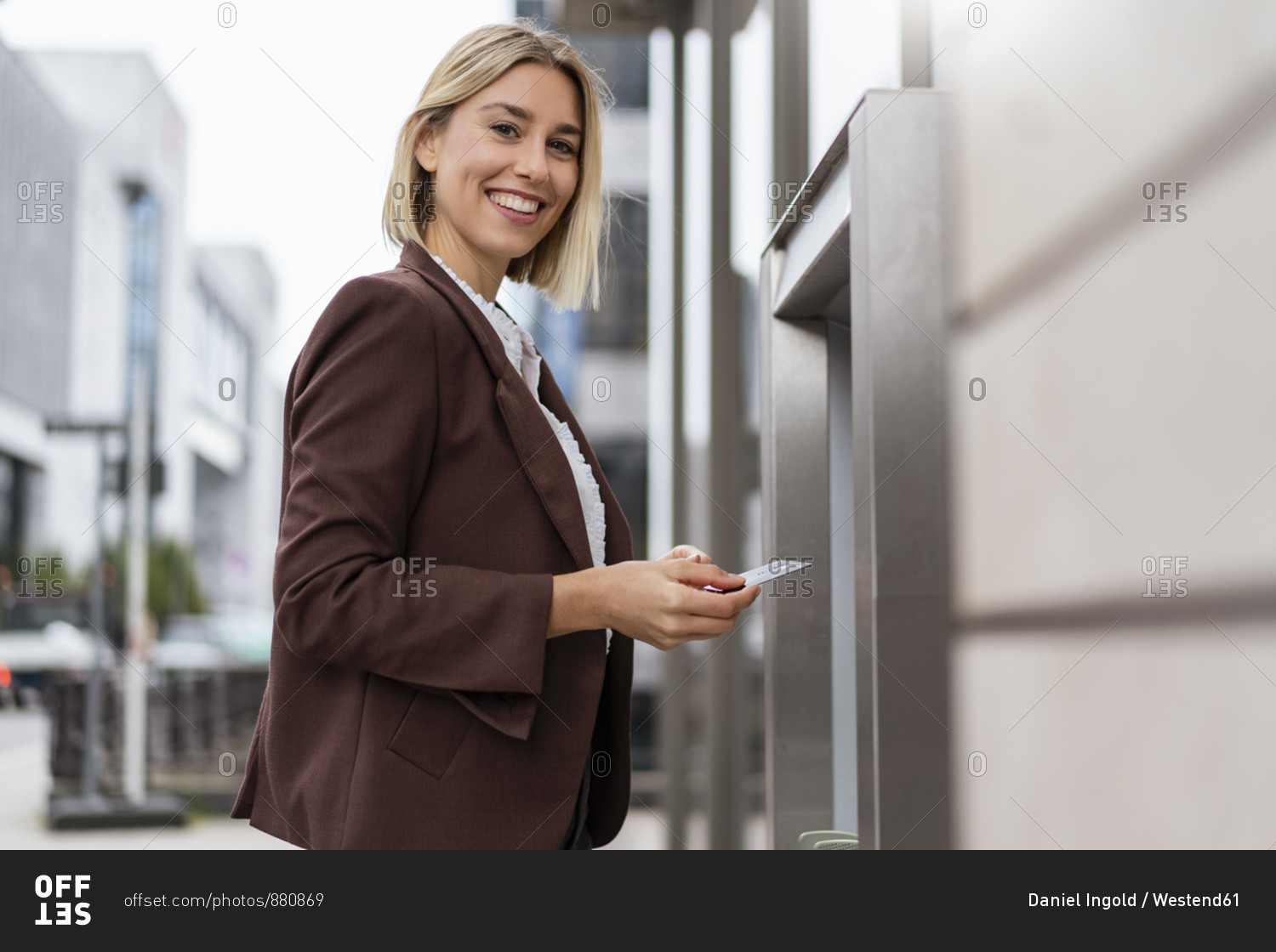 Portrait of smiling young businesswoman withdrawing money at an ATM in the city