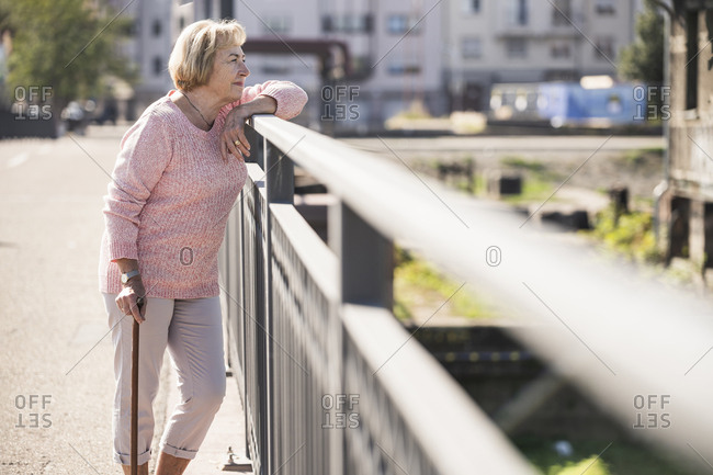 Senior woman walking on footbridge- using walking stick