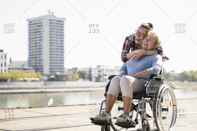 Young woman head to head with her laughing grandmother sitting in wheelchair