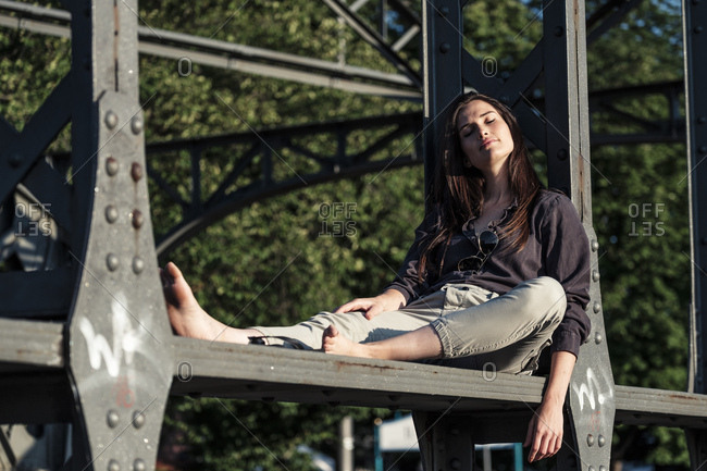 Young woman enjoying the evening sun- sitting on a bridge