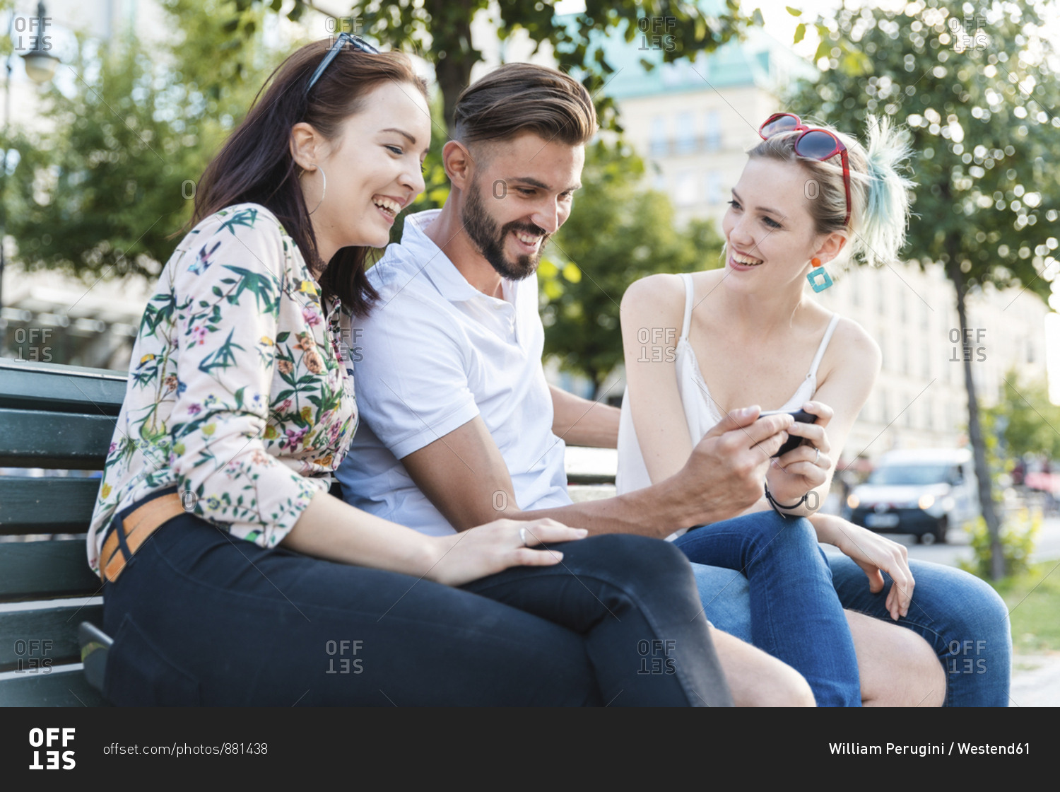 Three friends sitting together on a bench looking at cell phone stock ...